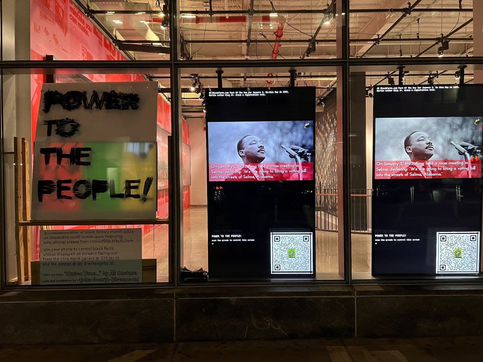 Storefront installation at 370 Jay Street: a hand-lettered POWER TO THE PEOPLE! sign and large digital monitors showing Black-history video content.